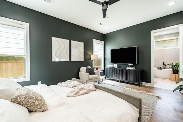 bedroom featuring multiple windows, hardwood / wood-style floors, ceiling fan, and ensuite bath