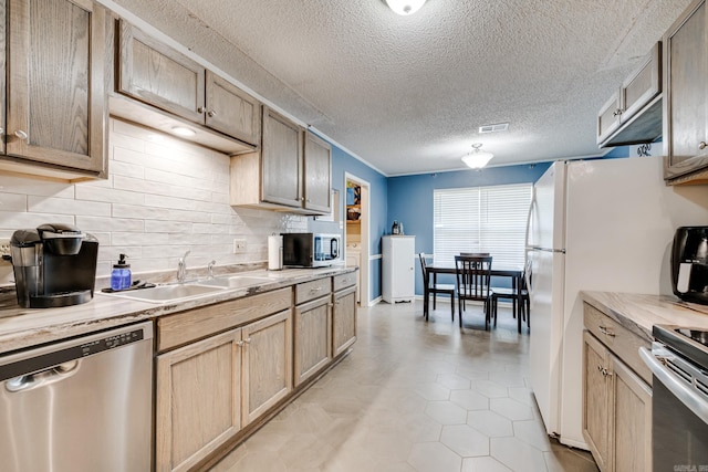 kitchen featuring a textured ceiling, appliances with stainless steel finishes, light tile patterned flooring, sink, and backsplash