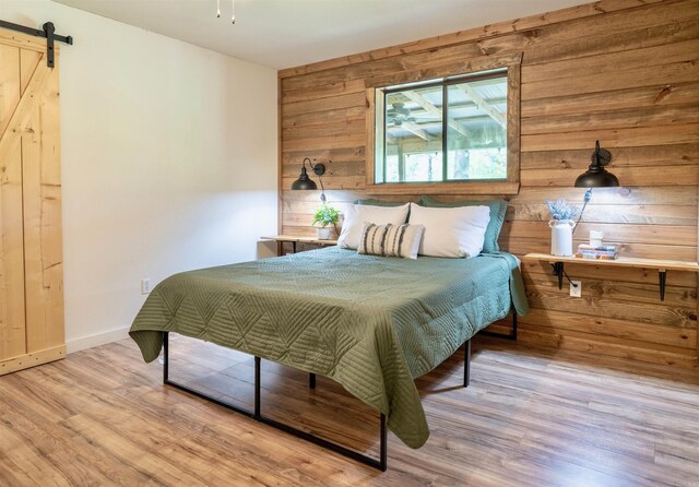 bedroom featuring light wood-type flooring, wooden walls, and a barn door