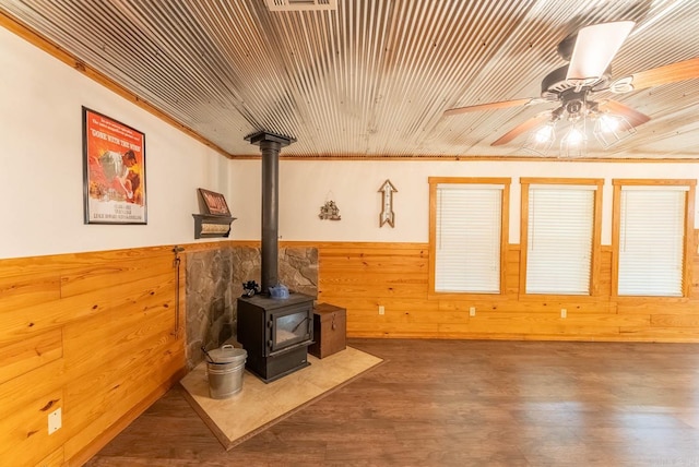 interior space featuring wood walls, ornamental molding, a wood stove, wood-type flooring, and ceiling fan