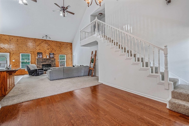 living room with ceiling fan, a stone fireplace, high vaulted ceiling, hardwood / wood-style floors, and track lighting