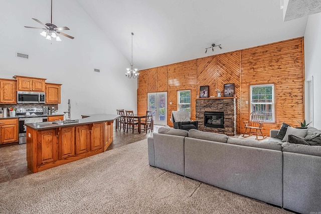 living room featuring dark tile patterned floors, a fireplace, wooden walls, high vaulted ceiling, and ceiling fan with notable chandelier