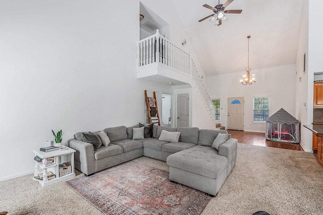 carpeted living room with high vaulted ceiling and ceiling fan with notable chandelier