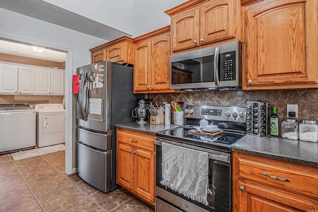 kitchen with washer and dryer, appliances with stainless steel finishes, decorative backsplash, and dark tile patterned floors