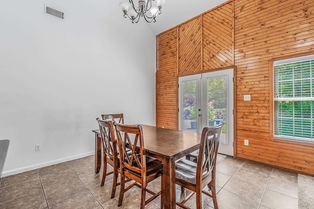 tiled dining space featuring wooden walls, high vaulted ceiling, a chandelier, and french doors