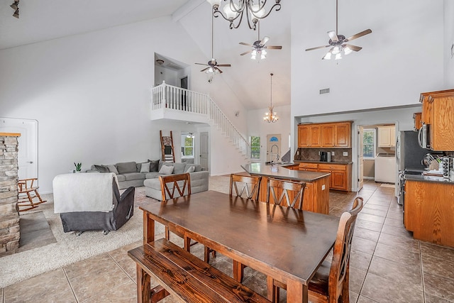 dining space with sink, beamed ceiling, high vaulted ceiling, ceiling fan with notable chandelier, and light tile patterned floors