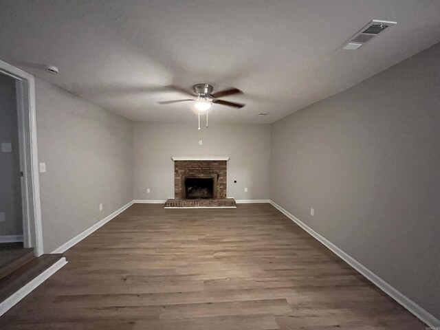 unfurnished living room with a brick fireplace, wood-type flooring, and ceiling fan