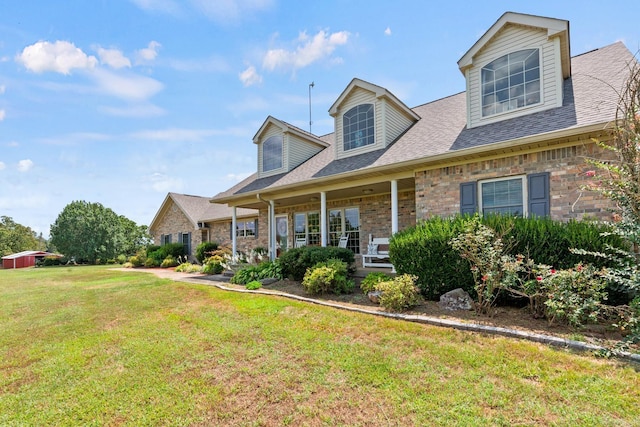 cape cod house featuring a shingled roof, a front lawn, and brick siding