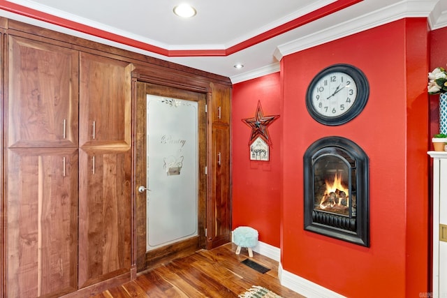 entryway with wood finished floors, visible vents, baseboards, a lit fireplace, and crown molding