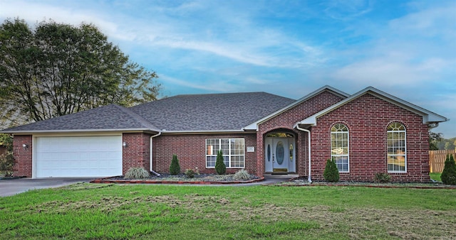 view of front of property featuring driveway, a garage, a shingled roof, a front yard, and brick siding