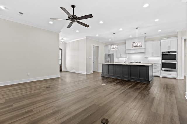 kitchen with decorative light fixtures, white cabinets, decorative backsplash, stainless steel appliances, and a center island with sink