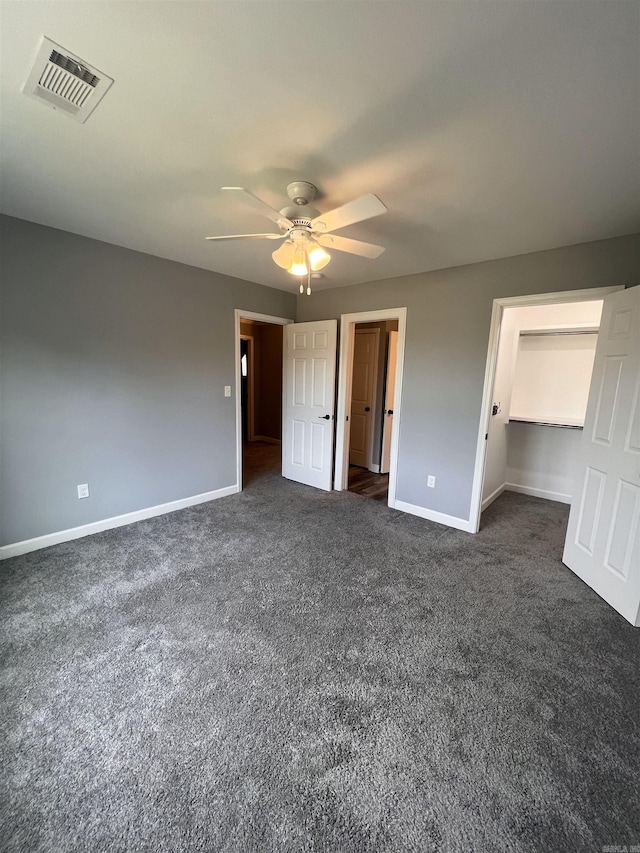 unfurnished bedroom with dark colored carpet, a closet, a walk in closet, and ceiling fan