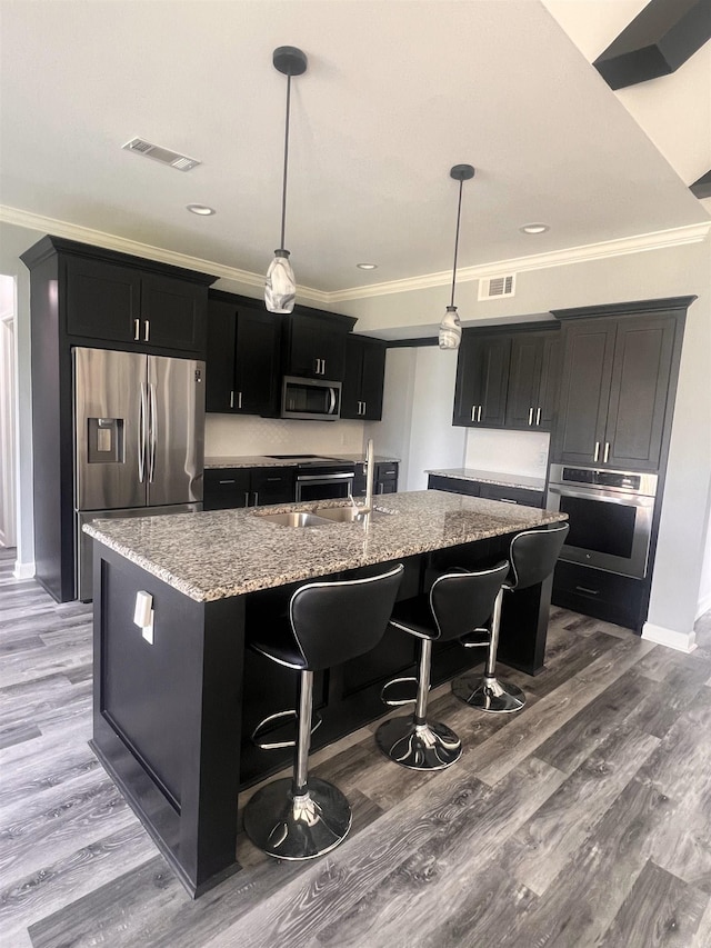 kitchen featuring hardwood / wood-style flooring, light stone counters, appliances with stainless steel finishes, and an island with sink