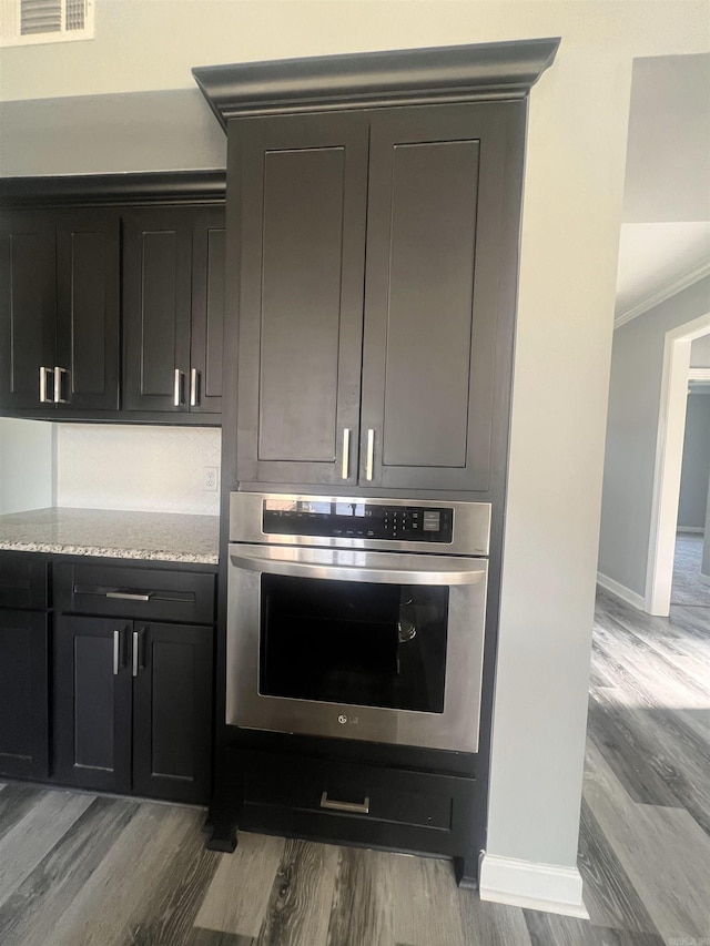 kitchen with light hardwood / wood-style flooring, crown molding, light stone counters, and stainless steel oven