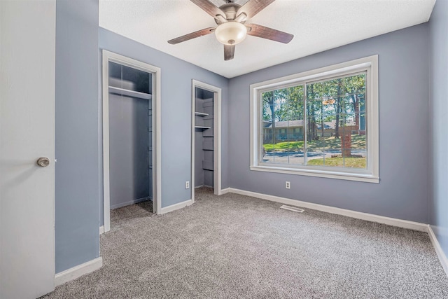 unfurnished bedroom with ceiling fan, light carpet, and two closets