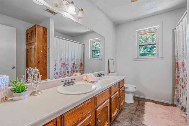 bathroom featuring toilet, dual bowl vanity, tile patterned flooring, and a healthy amount of sunlight