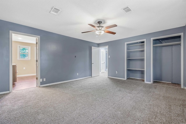 unfurnished bedroom featuring carpet floors, two closets, ceiling fan, and a textured ceiling