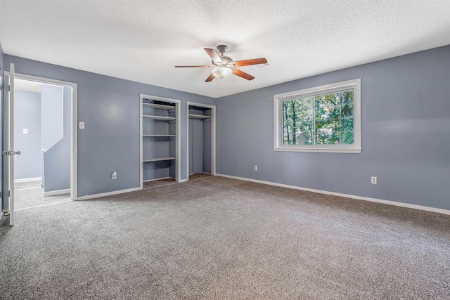 unfurnished bedroom with a textured ceiling, carpet flooring, ceiling fan, and two closets