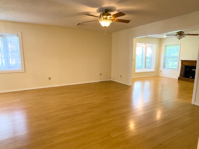 unfurnished living room featuring ceiling fan, light wood-type flooring, and a textured ceiling