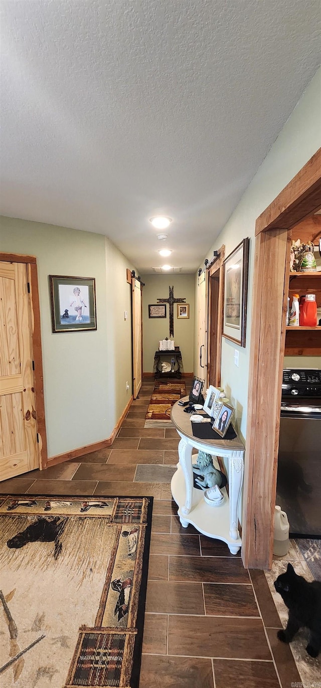 corridor featuring wood tiled floors, a textured ceiling, baseboards, and a barn door