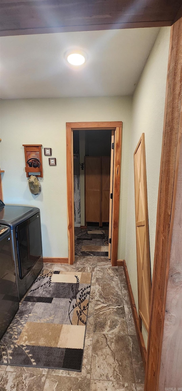 corridor featuring washer and dryer, baseboards, and stone finish floors