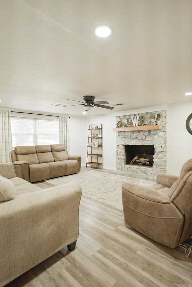 living room with ceiling fan, light hardwood / wood-style floors, and a stone fireplace