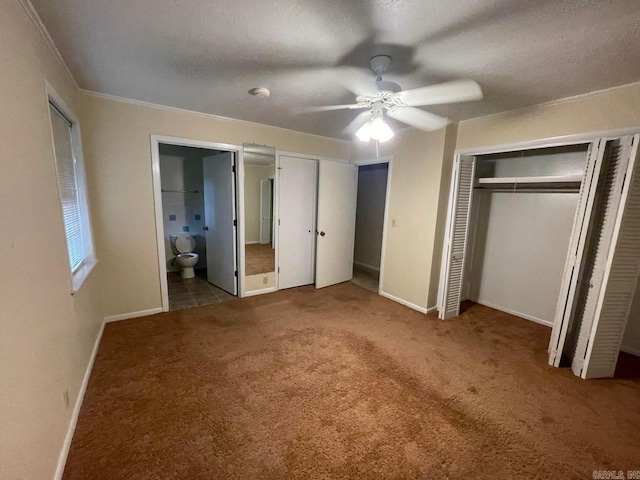 unfurnished bedroom with ceiling fan, two closets, carpet flooring, connected bathroom, and a textured ceiling