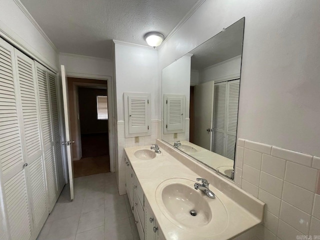 bathroom with ornamental molding, tile patterned floors, a textured ceiling, double vanity, and tile walls