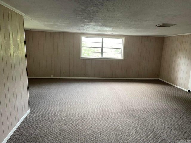 carpeted empty room featuring wood walls and a textured ceiling