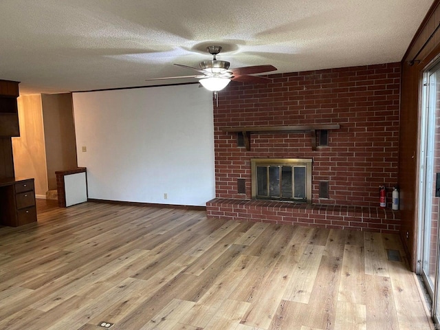 unfurnished living room with ceiling fan, light wood-type flooring, brick wall, a fireplace, and a textured ceiling