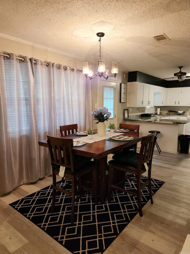 dining room with light wood-type flooring, visible vents, a textured ceiling, and ceiling fan with notable chandelier