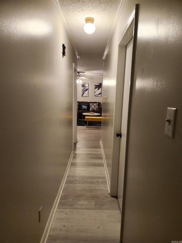 hallway with baseboards, ornamental molding, a textured ceiling, and wood finished floors