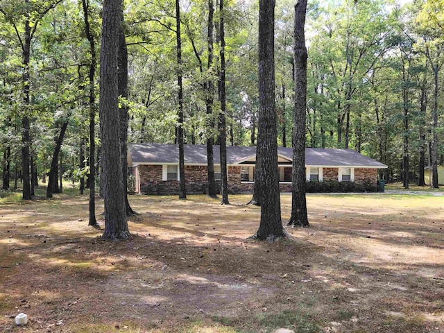 ranch-style home with a forest view and brick siding