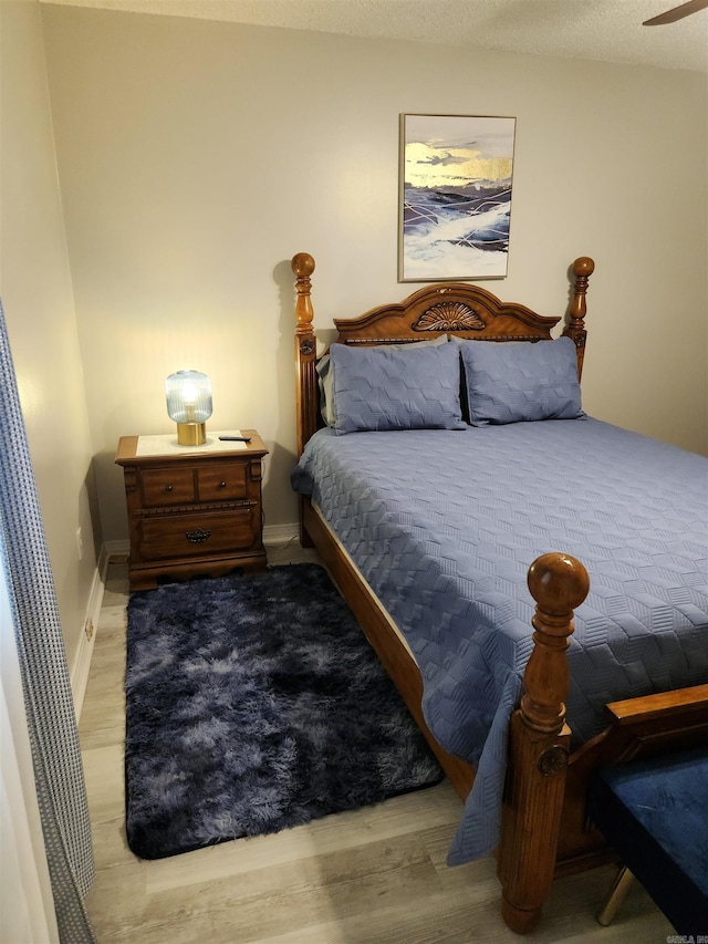 bedroom with a textured ceiling, baseboards, and wood finished floors