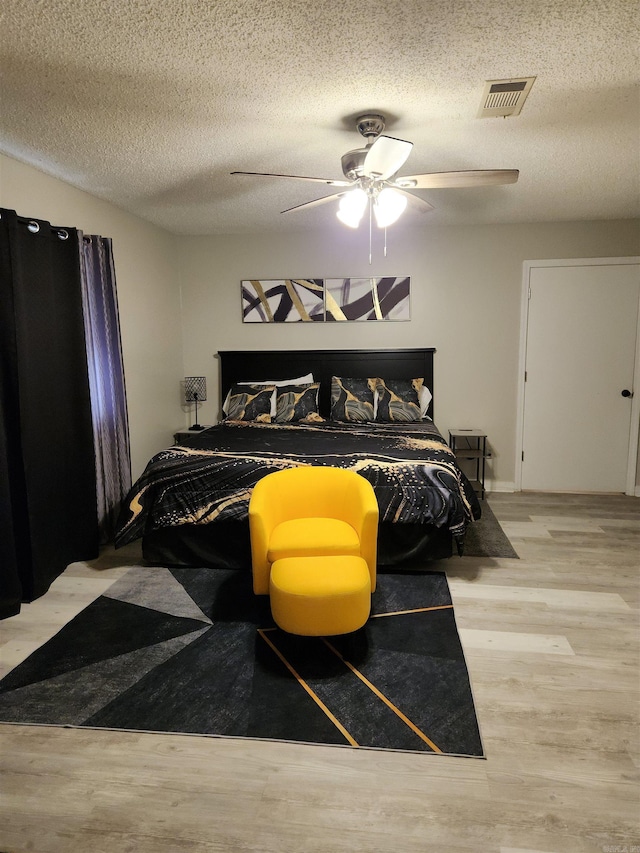 bedroom with ceiling fan, a textured ceiling, visible vents, and wood finished floors