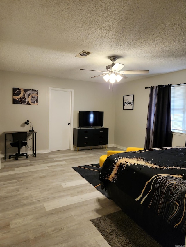 bedroom with visible vents, baseboards, a ceiling fan, light wood-style flooring, and a textured ceiling