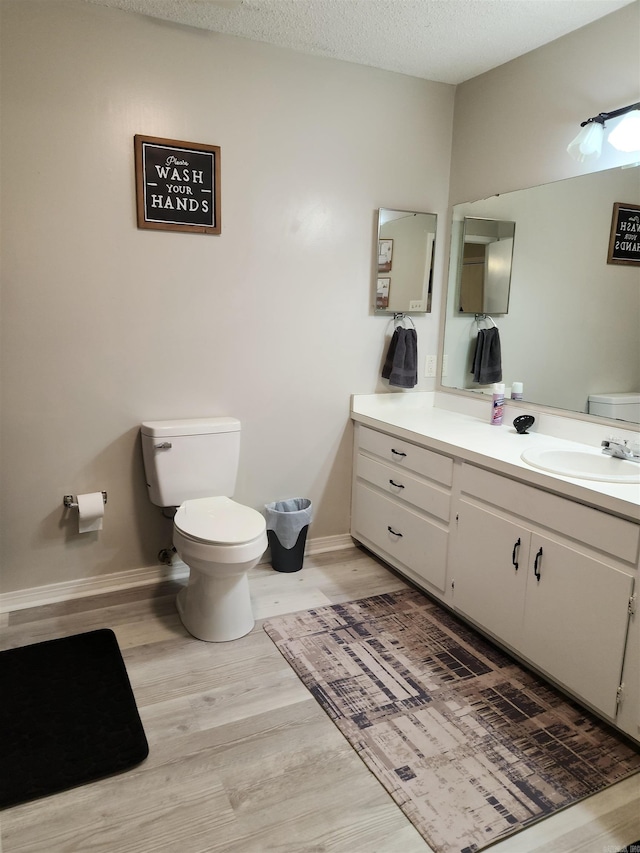 bathroom with baseboards, toilet, wood finished floors, a textured ceiling, and vanity