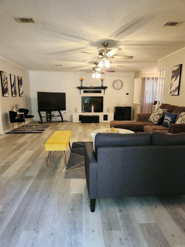 living room featuring a brick fireplace, visible vents, a textured ceiling, and wood finished floors