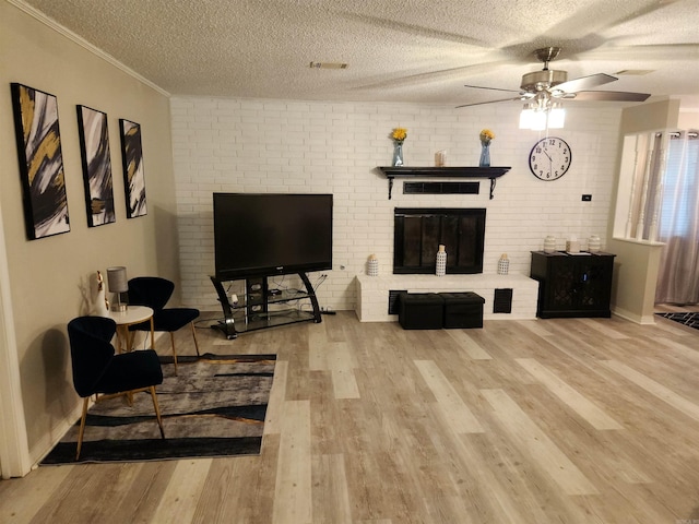 living area with visible vents, wood finished floors, a textured ceiling, crown molding, and a fireplace