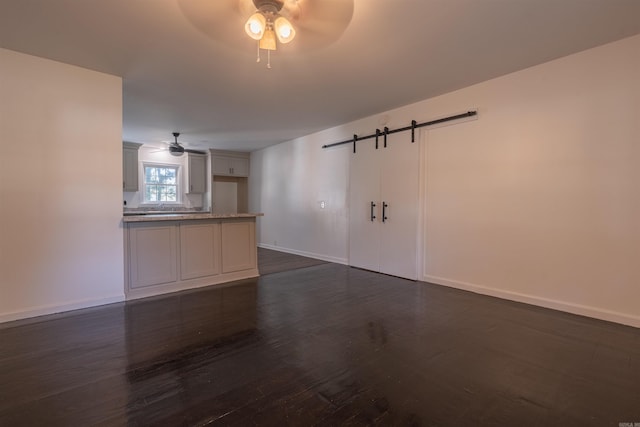 unfurnished room with ceiling fan, dark hardwood / wood-style floors, and a barn door