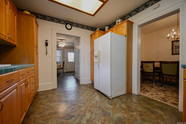 kitchen featuring tile counters, ceiling fan with notable chandelier, tile patterned floors, decorative light fixtures, and white fridge with ice dispenser