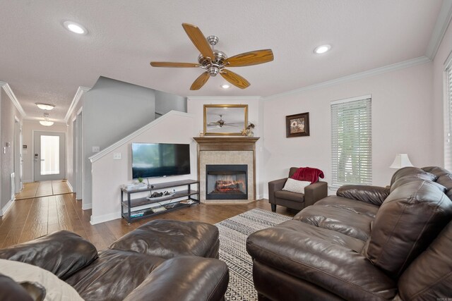 living room with ceiling fan, hardwood / wood-style flooring, ornamental molding, and a tile fireplace