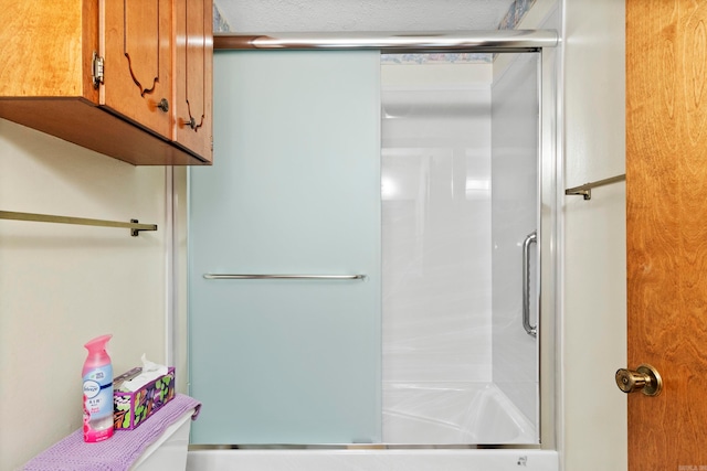 bathroom featuring a textured ceiling and bath / shower combo with glass door