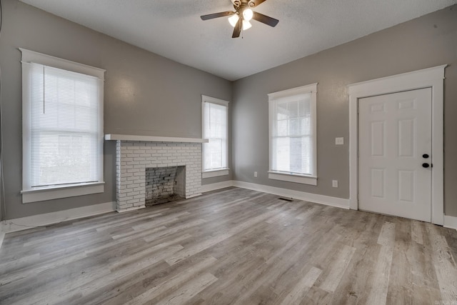 unfurnished living room featuring light hardwood / wood-style floors, ceiling fan, a brick fireplace, and a textured ceiling