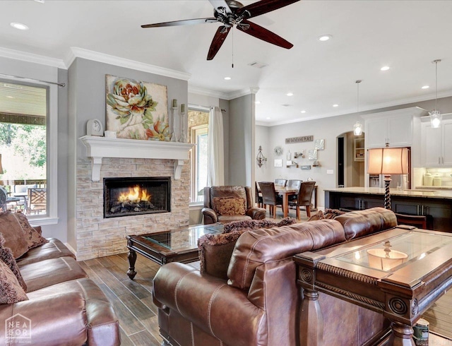 living room with a stone fireplace, ceiling fan, dark hardwood / wood-style flooring, and crown molding