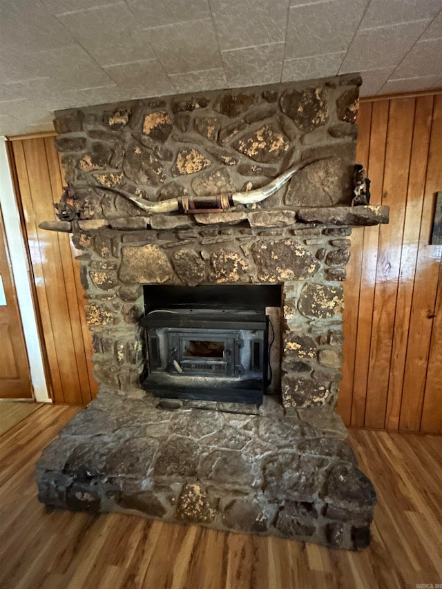 room details with wood walls, hardwood / wood-style flooring, and a stone fireplace