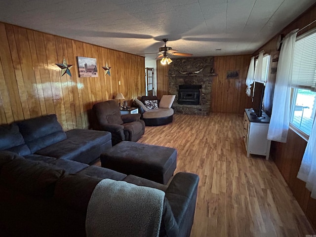 living room featuring hardwood / wood-style floors, a stone fireplace, ceiling fan, and wood walls