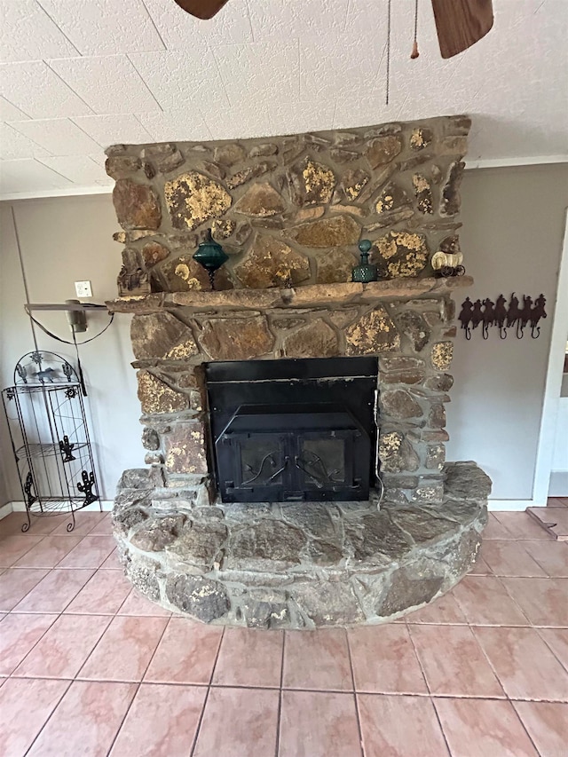 room details featuring ornamental molding, tile patterned floors, a textured ceiling, ceiling fan, and a stone fireplace