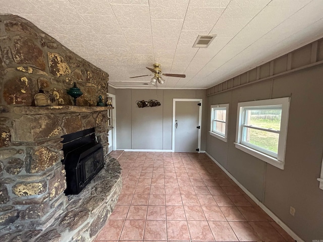 unfurnished living room with ceiling fan, light tile patterned flooring, and a stone fireplace