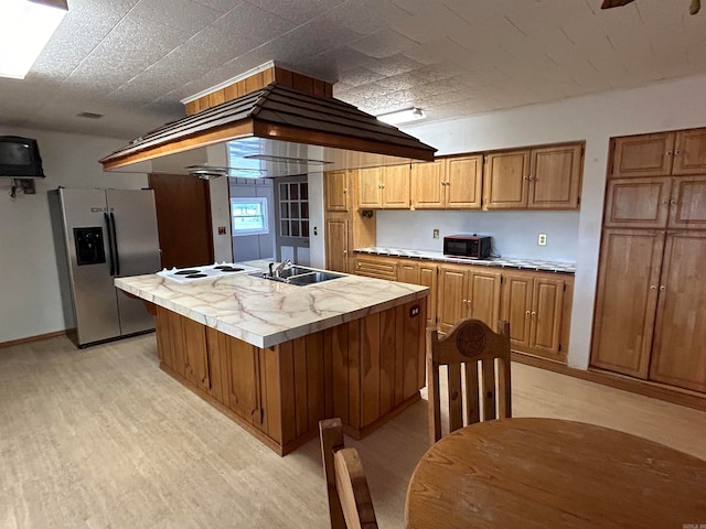 kitchen featuring light hardwood / wood-style flooring, sink, white electric cooktop, a kitchen island with sink, and stainless steel fridge